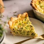 A slice of Air Fryer Vegan Asparagus Quiche with a golden crust sits on a white plate, with a fork beside it.