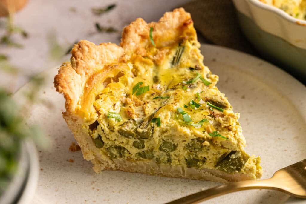 A close-up of Air Fryer Vegan Asparagus Quiche with a golden crust, garnished with chopped herbs, served on a plate with a fork.