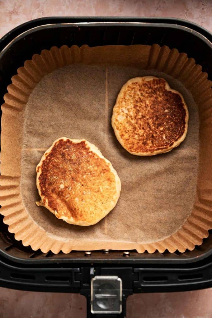 Two Air Fryer Vegan Pancakes rest on parchment paper inside the basket, with one pancake slightly darker than the other.