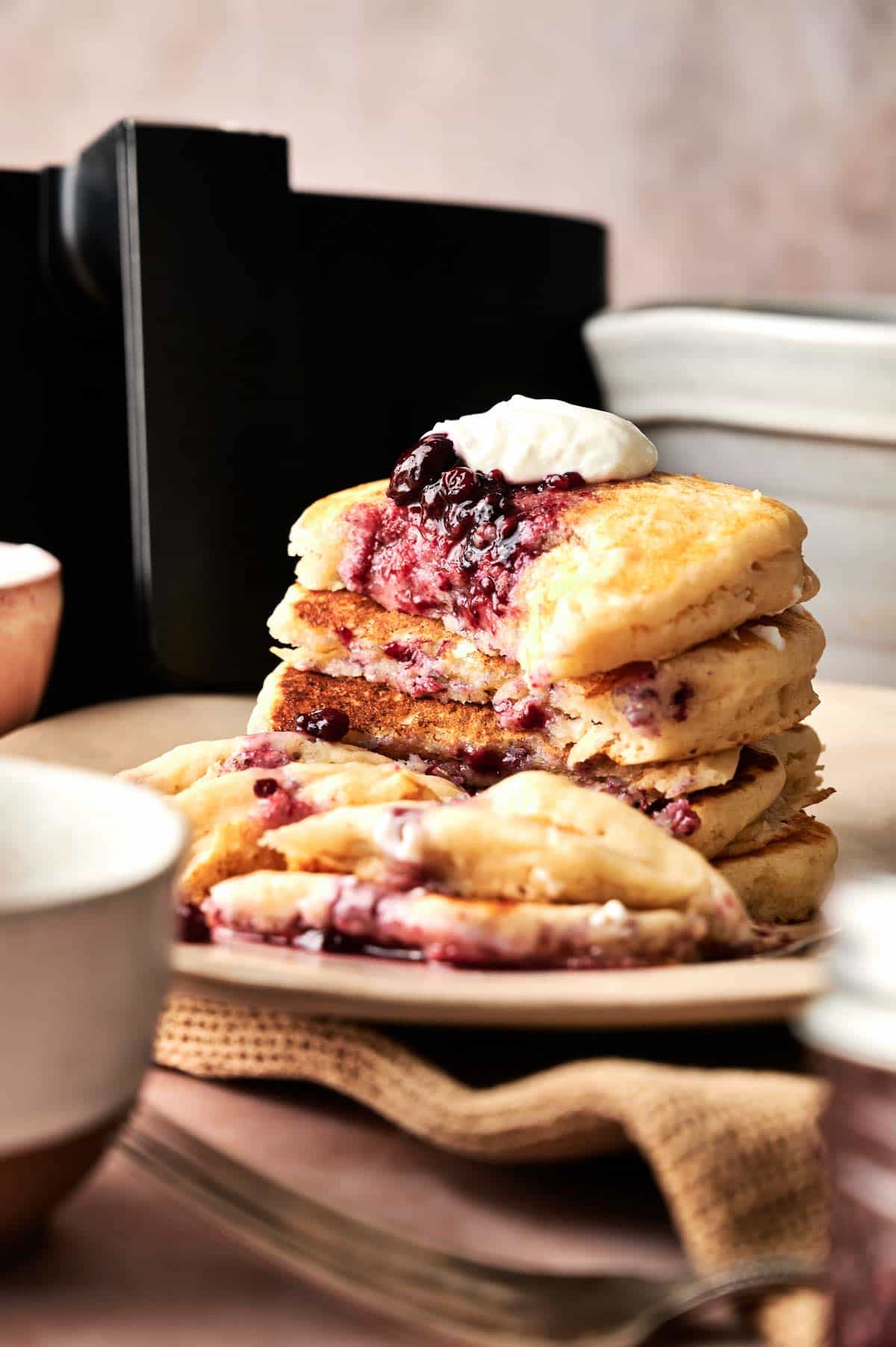 A stack of Air Fryer Vegan Pancakes topped with berry compote and cream, with a portion cut out to reveal the fluffy interior and luscious berry filling.