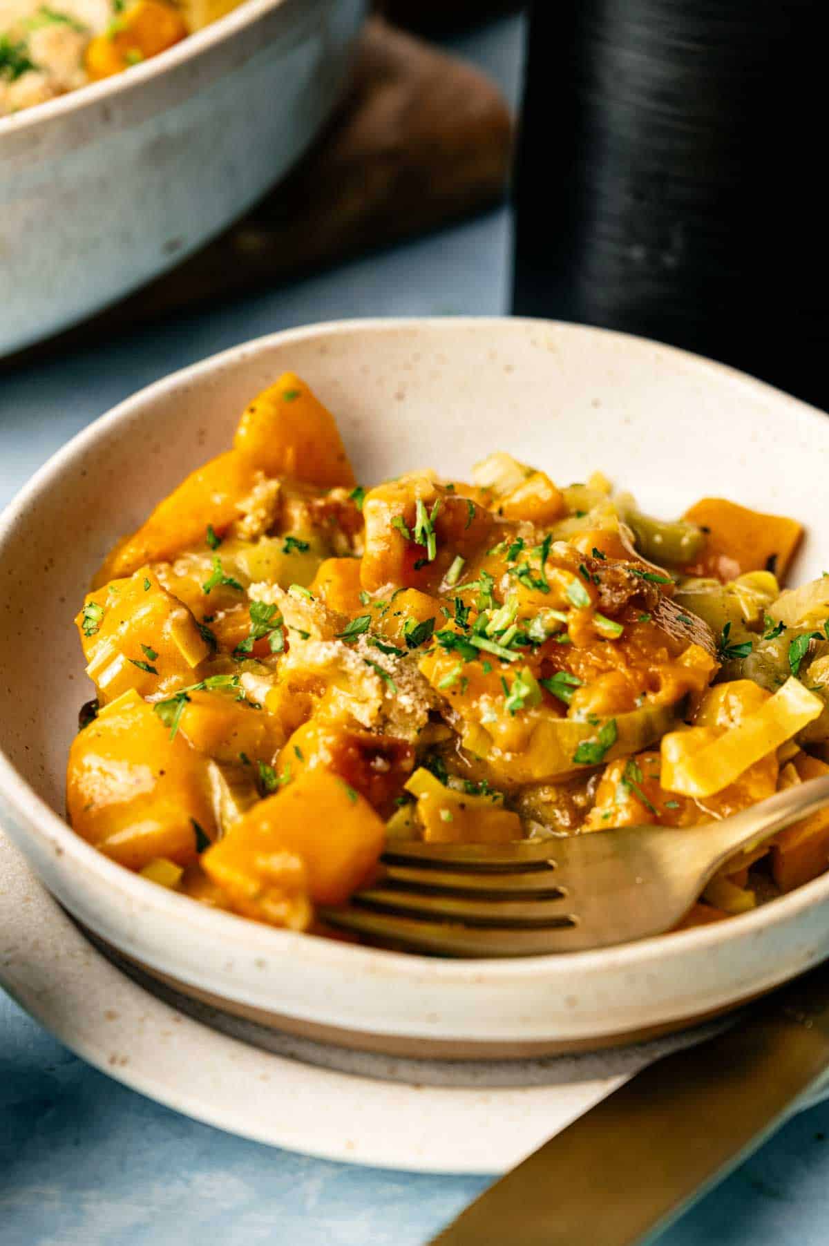 A bowl of cooked butternut squash mixed with herbs and garnished with chopped parsley, served with a fork&mdash;perfect as an Air Fryer Vegan Squash Casserole.