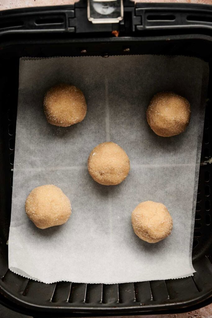 Five dough balls for Air Fryer Vegan Sugar Cookies are placed on a sheet of parchment paper inside an air fryer basket, ready to be cooked.