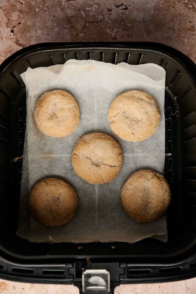 Five round Air Fryer Vegan Sugar Cookies are arranged on a sheet of parchment paper inside an air fryer basket.