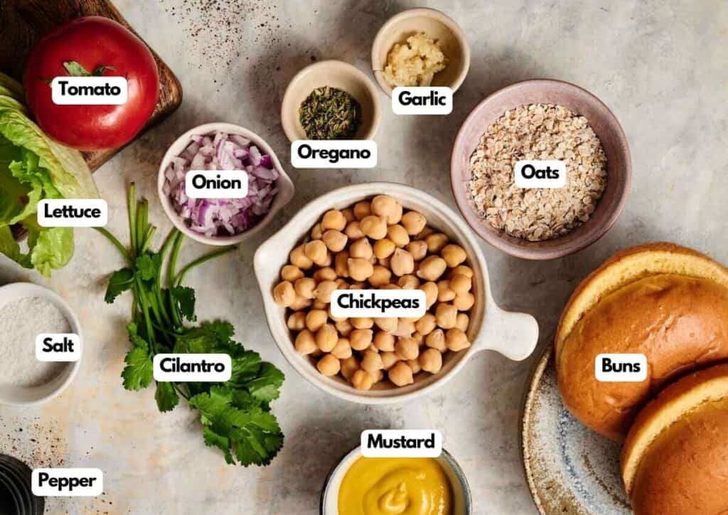 A variety of ingredients on a table, including chopped onion, tomato, lettuce, cilantro, oats, buns, mustard, garlic, oregano, salt, and pepper&mdash;perfect for making delicious Air Fryer Chickpea Burgers.