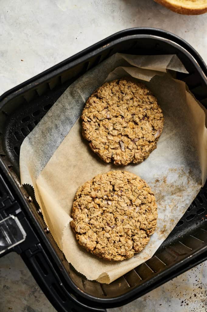 Two oatmeal cookies rest on parchment paper inside an air fryer basket, ready to be enjoyed after making a batch of Air Fryer Chickpea Burgers.