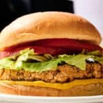 A close-up of an Air Fryer Chickpea Burger with lettuce, tomato, and mustard on a bun, placed on a white plate.