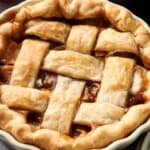 A close-up of an Air Fryer Vegan Apple Pie with a golden brown lattice crust and visible fruit filling in a white pie dish.