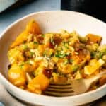 A bowl of cooked butternut squash pasta with herbs and cheese, inspired by Air Fryer Vegan Squash Casserole, served in a cream-colored dish with a fork.