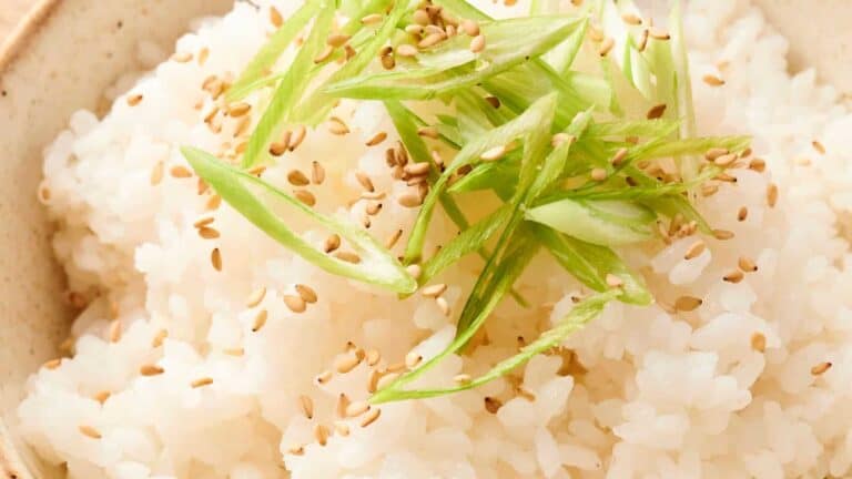A close-up of white rice topped with sliced green onions and sprinkled with sesame seeds.