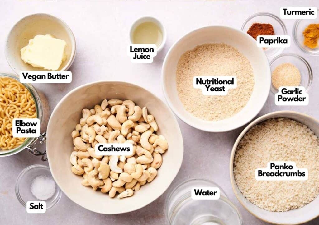 A top-down view of labeled ingredients for Air Fryer Mac and Cheese, including cashews, vegan butter, nutritional yeast, spices, panko breadcrumbs, pasta, water, salt, and lemon juice.