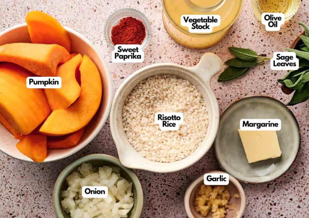 Assorted ingredients for Air Fryer Pumpkin Risotto arranged on a countertop, including pumpkin, risotto rice, onion, garlic, margarine, sage leaves, sweet paprika, vegetable stock, and olive oil.