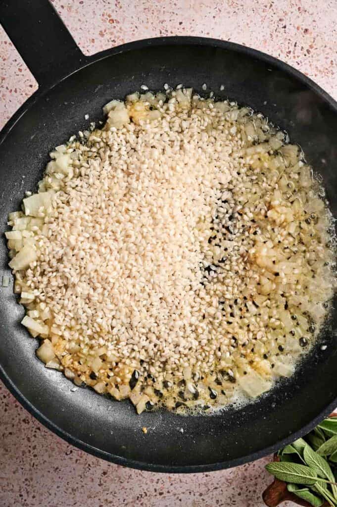 Chopped onions and uncooked Arborio rice saut&eacute;ing in oil in a black pan, the perfect start for a creamy Air Fryer Pumpkin Risotto.