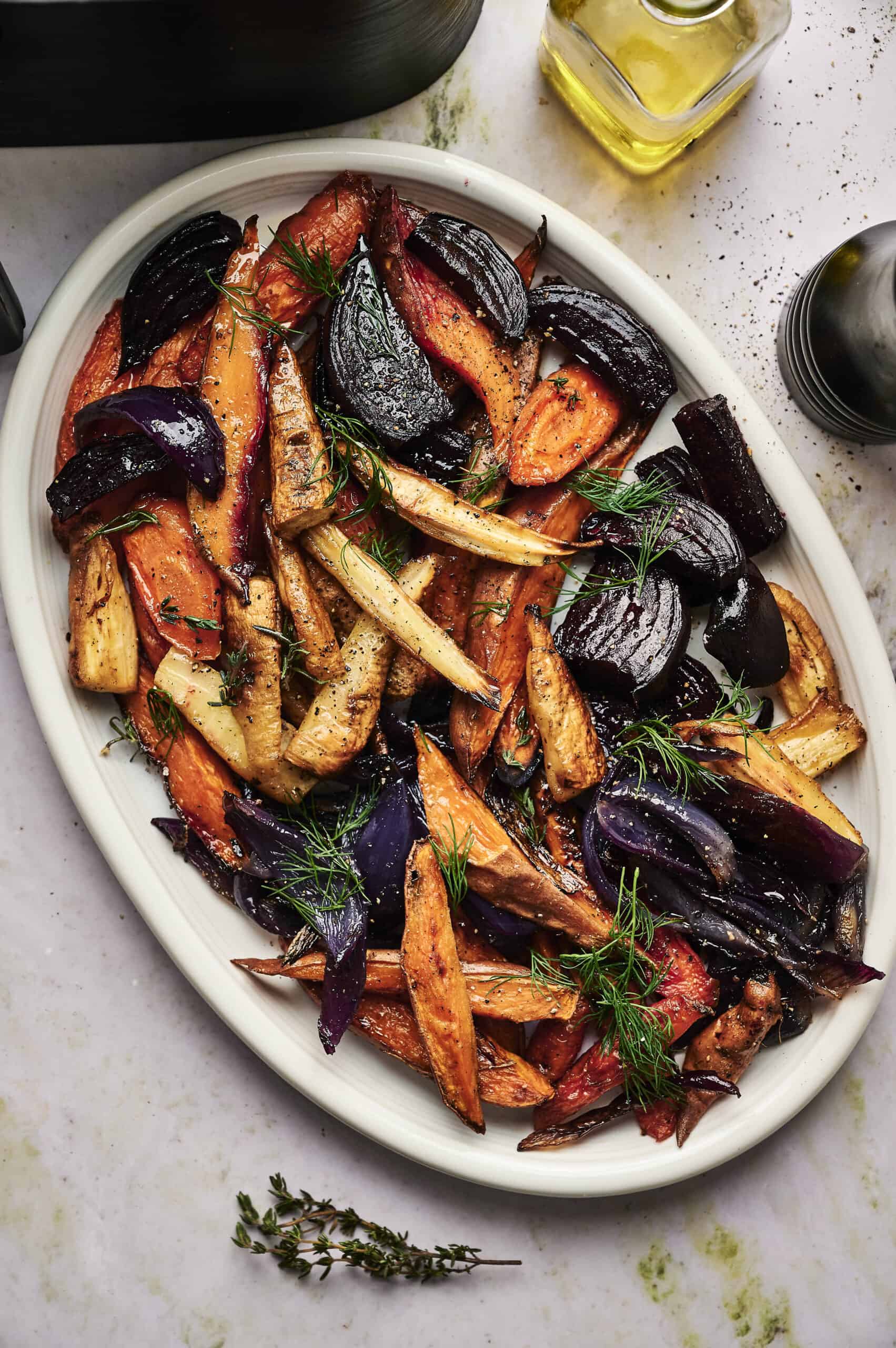 A white oval platter filled with Air Fryer Roasted Root Vegetables, including carrots, parsnips, and beets, all perfectly crisp and garnished with fresh herbs.
