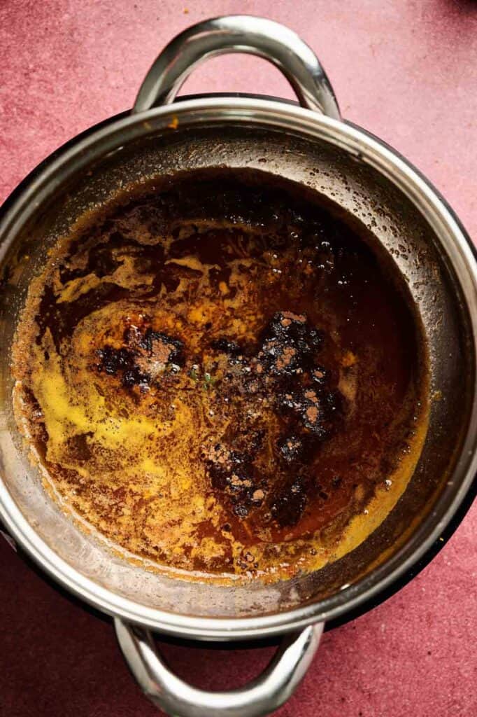 A stainless steel pot containing browned butter with dark brown bits and foam on the surface, set on a reddish countertop—perfectly prepared to add rich flavor to Sweet Potato Casserole with Orange Juice.