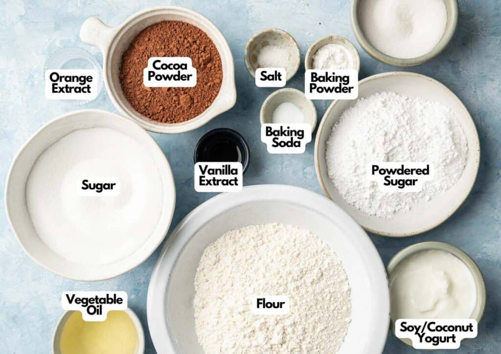 Various baking ingredients in bowls and cups labeled: orange extract, cocoa powder, salt, baking soda, flour, vegetable oil, sugar, vanilla extract, soy/coconut yogurt&mdash;perfect for making Air Fryer Vegan Crinkle Cookies.