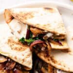 Close-up of Vegan Quesadillas with Mushroom Bacon, filled with melted cheese, sautéed onions, mushrooms, and greens, served on a white plate.