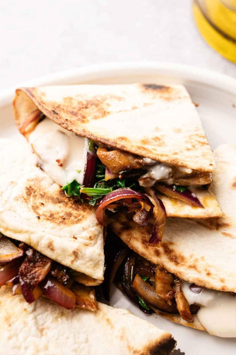 Close-up of Vegan Quesadillas with Mushroom Bacon, filled with melted cheese, sautéed onions, mushrooms, and greens, served on a white plate.