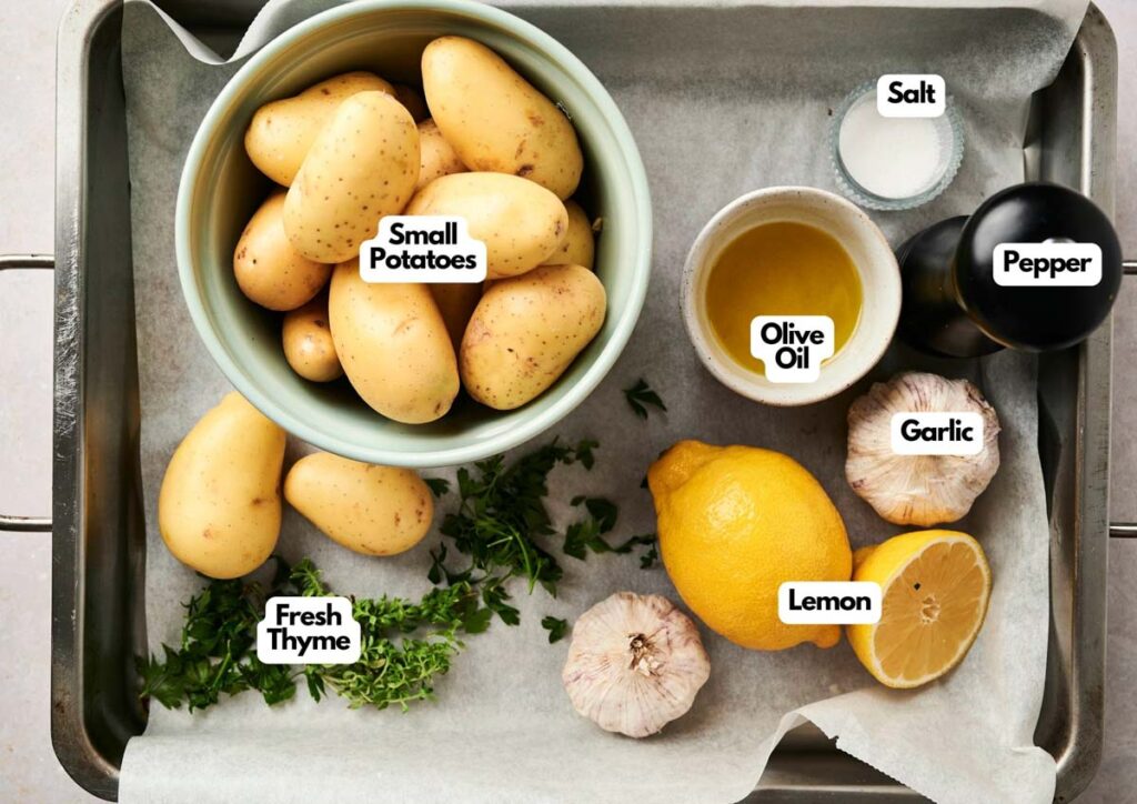 A baking tray with Air Fryer Vegan Roasted Potatoes, fresh thyme, garlic, a halved lemon, olive oil, salt, and pepper&mdash;each ingredient labeled for easy prep.