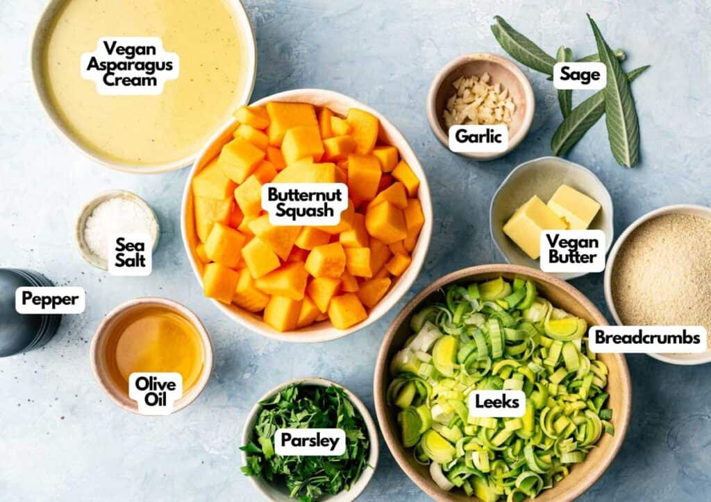 A variety of labeled ingredients on a countertop, perfect for making Air Fryer Vegan Squash Casserole: butternut squash, leeks, vegan asparagus cream, vegan butter, breadcrumbs, garlic, sage, olive oil, parsley, sea salt, and pepper.