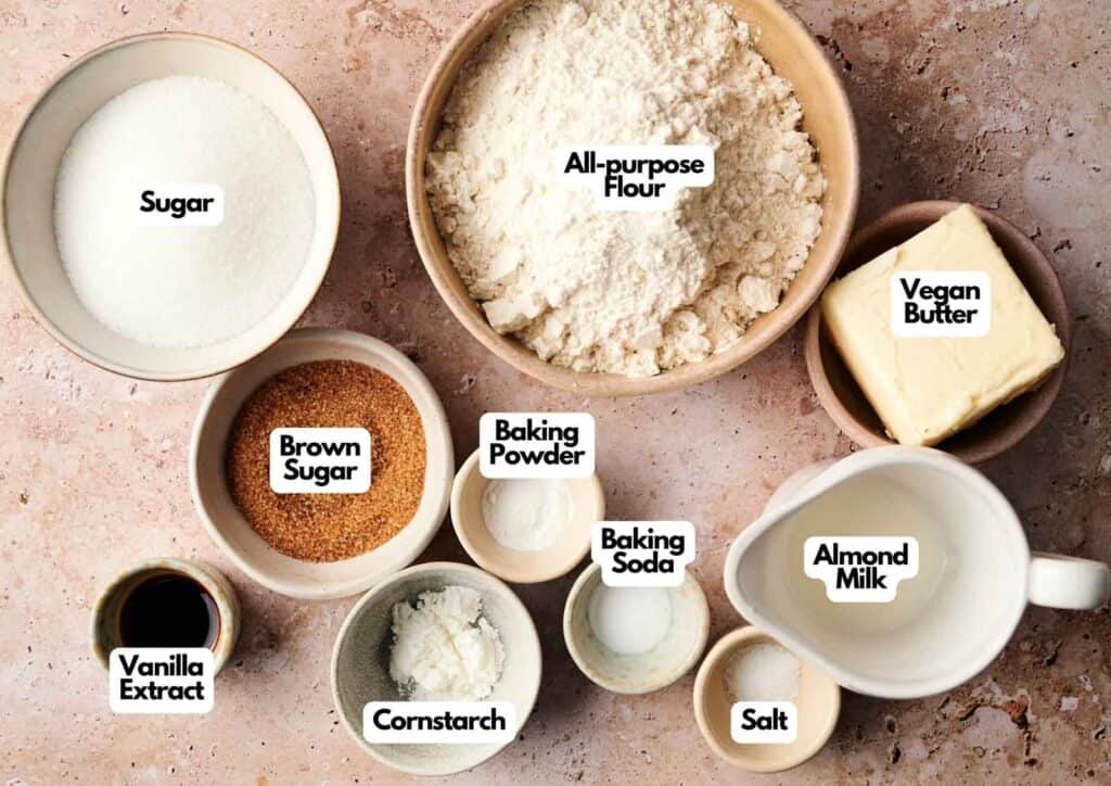 Various labeled baking ingredients in bowls and cups, perfect for making Air Fryer Vegan Sugar Cookies&mdash;includes all-purpose flour, vegan butter, almond milk, sugars, cornstarch, baking powder, baking soda, vanilla extract, and salt.