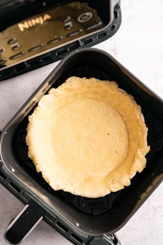 Unbaked pie crust placed inside an air fryer basket, ready for cooking a delicious Air Fryer Vegan Asparagus Quiche.
