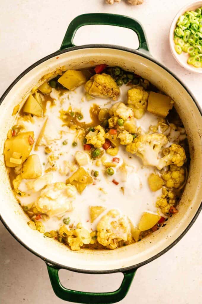 A pot of coconut curry vegetable delight with cauliflower, potatoes, peas, and other vegetables simmering in a creamy sauce.