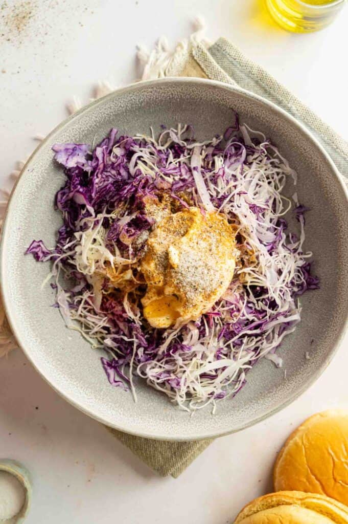 A bowl containing shredded purple and white cabbage topped with mayonnaise, mustard, and ground black pepper—perfect as a crisp, tangy side for Vegan BBQ Pulled Jackfruit Sandwiches.