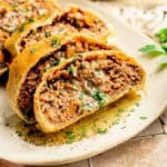 Sliced savory Vegan Wellington pastry filled with minced meat and vegetables, garnished with chopped parsley, served on a white plate.